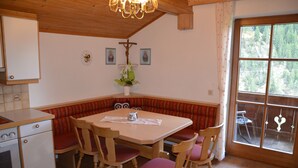 A cozy kitchen with wooden cabinets, a dining table with chairs, and a large window with a view of trees.