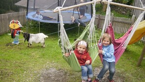 A hammock swing in a backyard with a trampoline and a goat nearby.