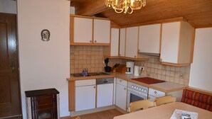 A compact kitchen with wooden cabinets, a stove, and a dining area with a table and chairs.