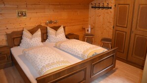A wooden bedroom with two beds, a nightstand, a small stool, and a wardrobe.