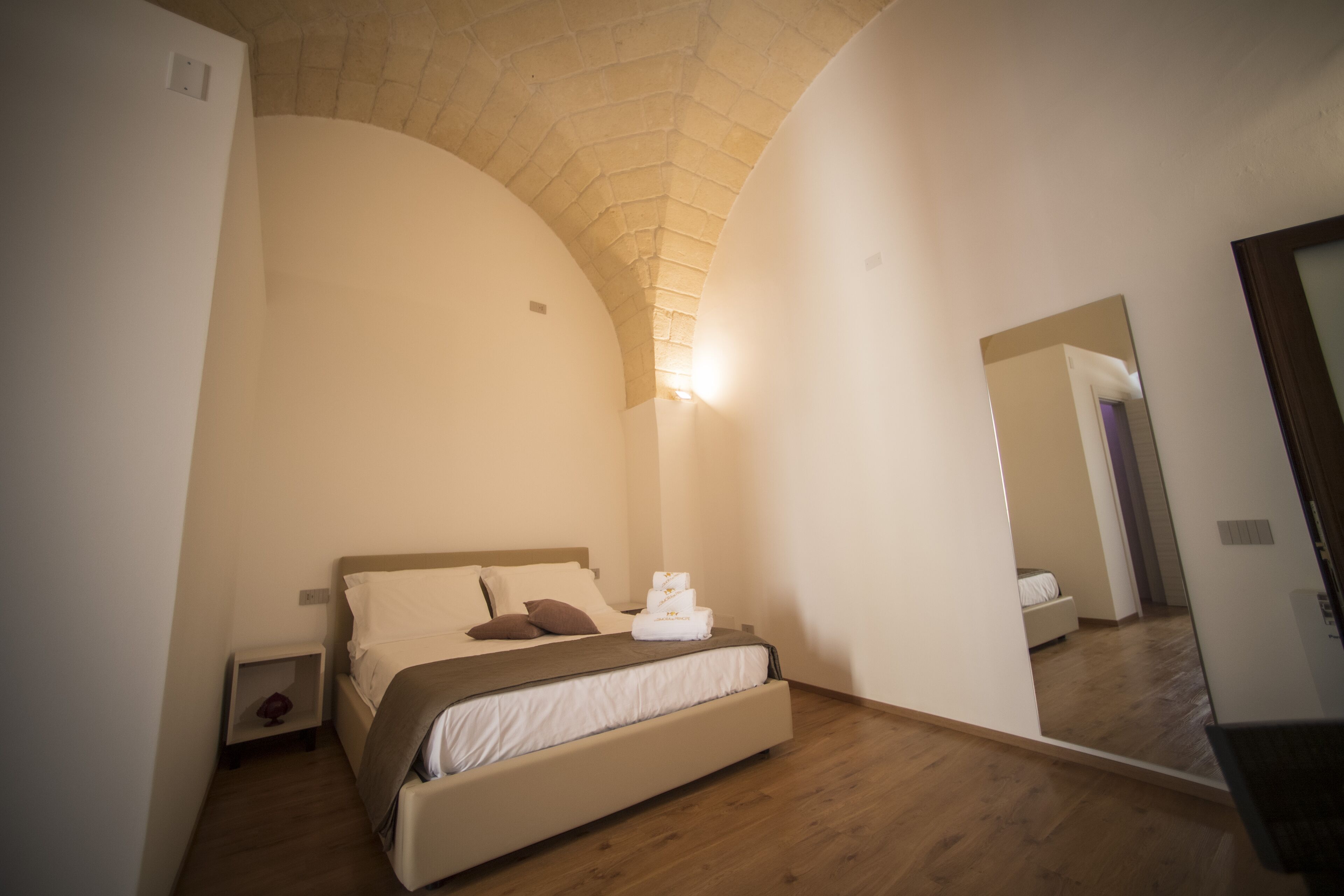 Un dormitorio con cama, mesita de noche, espejo y suelo de madera.
