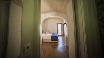 A narrow hallway leading to a bedroom with a single bed, a small window, and a door leading to another room.