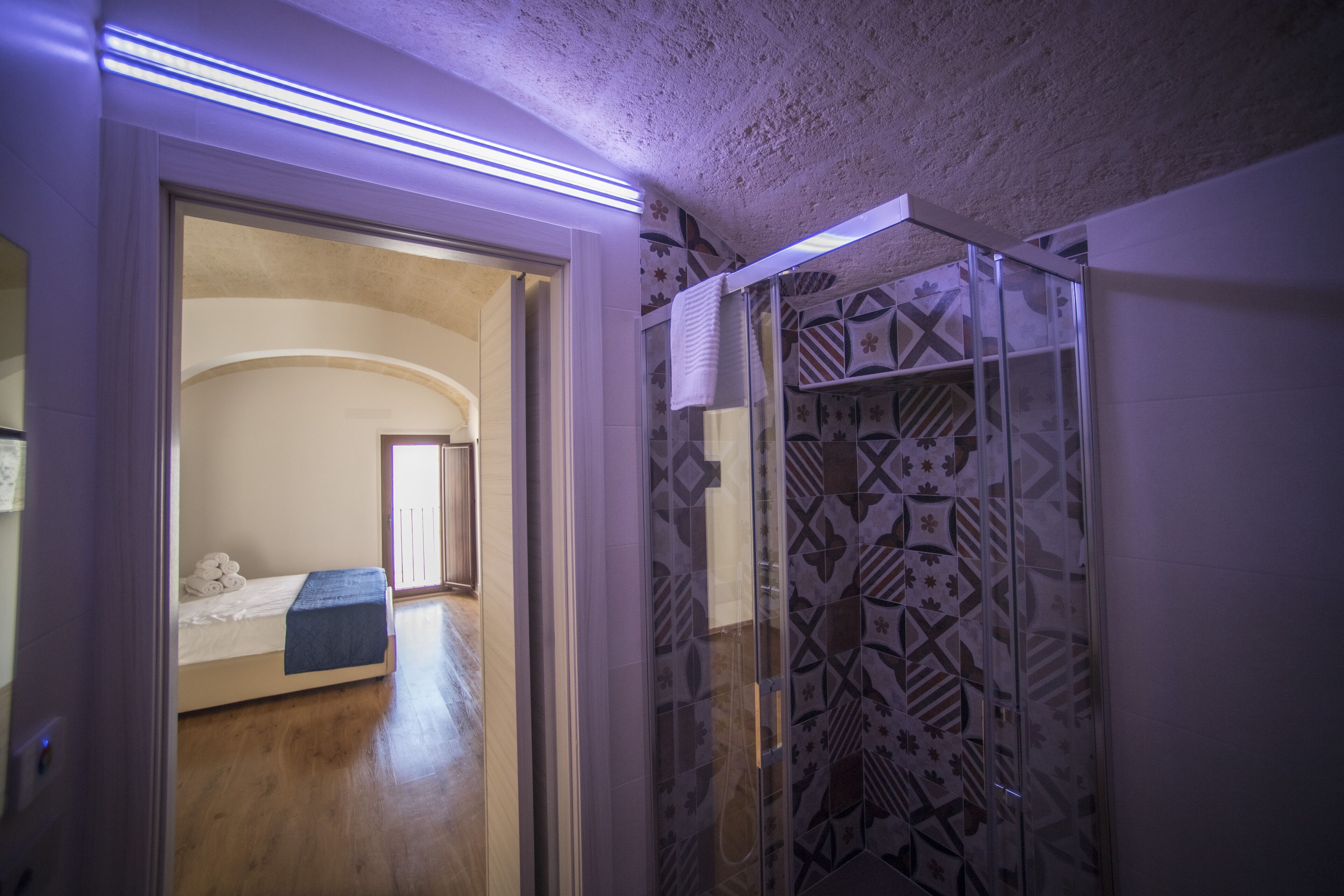 Una habitación con cama, un pequeño banco y cabina de ducha con diseño.
