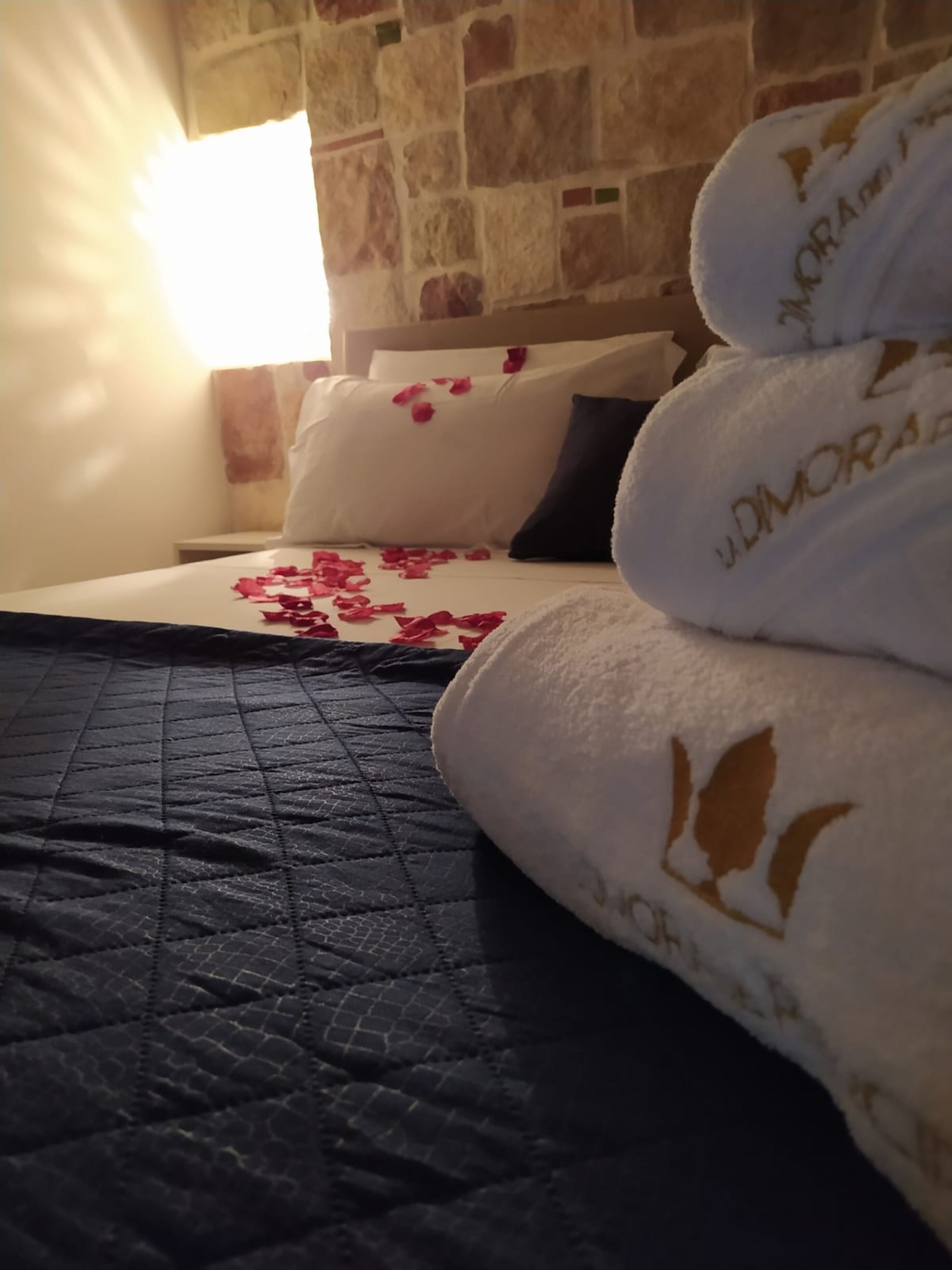 Una cama con un edredón oscuro, almohadas con estampado de rosas y una toalla con diseño de pájaro.
