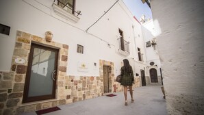 A narrow street with white buildings, stone walls, and a woman walking. - La Dimora del Principe (Grottaglie)