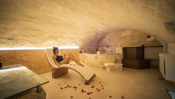 A spa room with a stone ceiling, a massage table, a stone bench, and a small stone fountain. - La Dimora del Principe (Grottaglie)