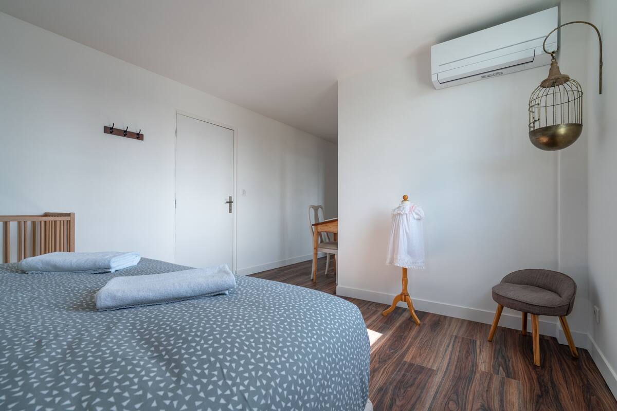 A bedroom with a bed, a chair, a small table, and a hanging light fixture.