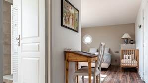 Una habitación con una mesa de comedor de madera, una silla blanca, una cuna y una lámpara en una mesita de noche.