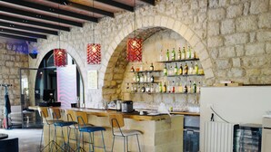 Zona de bar amb paret de pedra, barra de fusta i seients blaus.