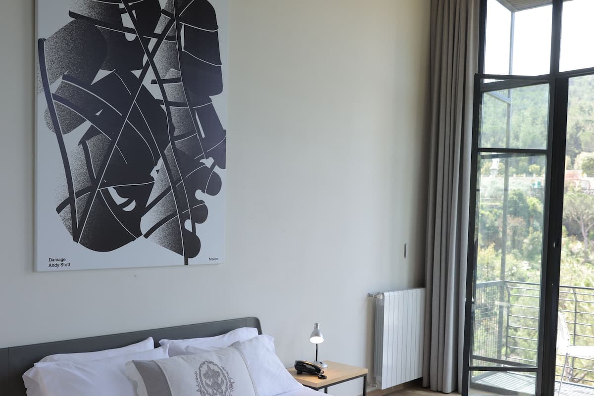 A modern hotel room with a large bed, a nightstand, a window with curtains, and a city view.