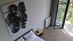 A modern hotel room with a large bed, a view of greenery through the window, and a contemporary abstract painting on the wall. - The Silk Valley Resort (Aarbaniye)