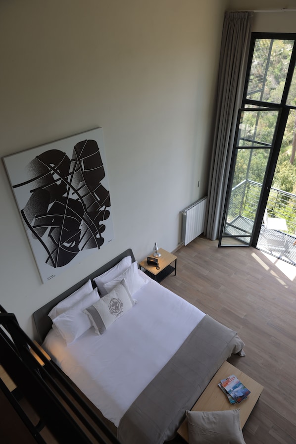 A modern hotel room with a large bed, a view of greenery through the window, and a contemporary abstract painting on the wall. - The Silk Valley Resort (Aarbaniye)