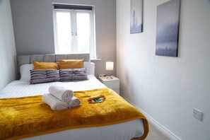 A neatly made bed with a yellow throw blanket, a bedside lamp, and a window with blinds. - Contractorscleancharming 2-bed House in Coventry (Coventry)