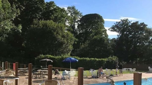 A pool area with wicker chairs and tables, surrounded by trees. - Upper Lake Chalet , Dog and Pet Friendly (Caernarfon)