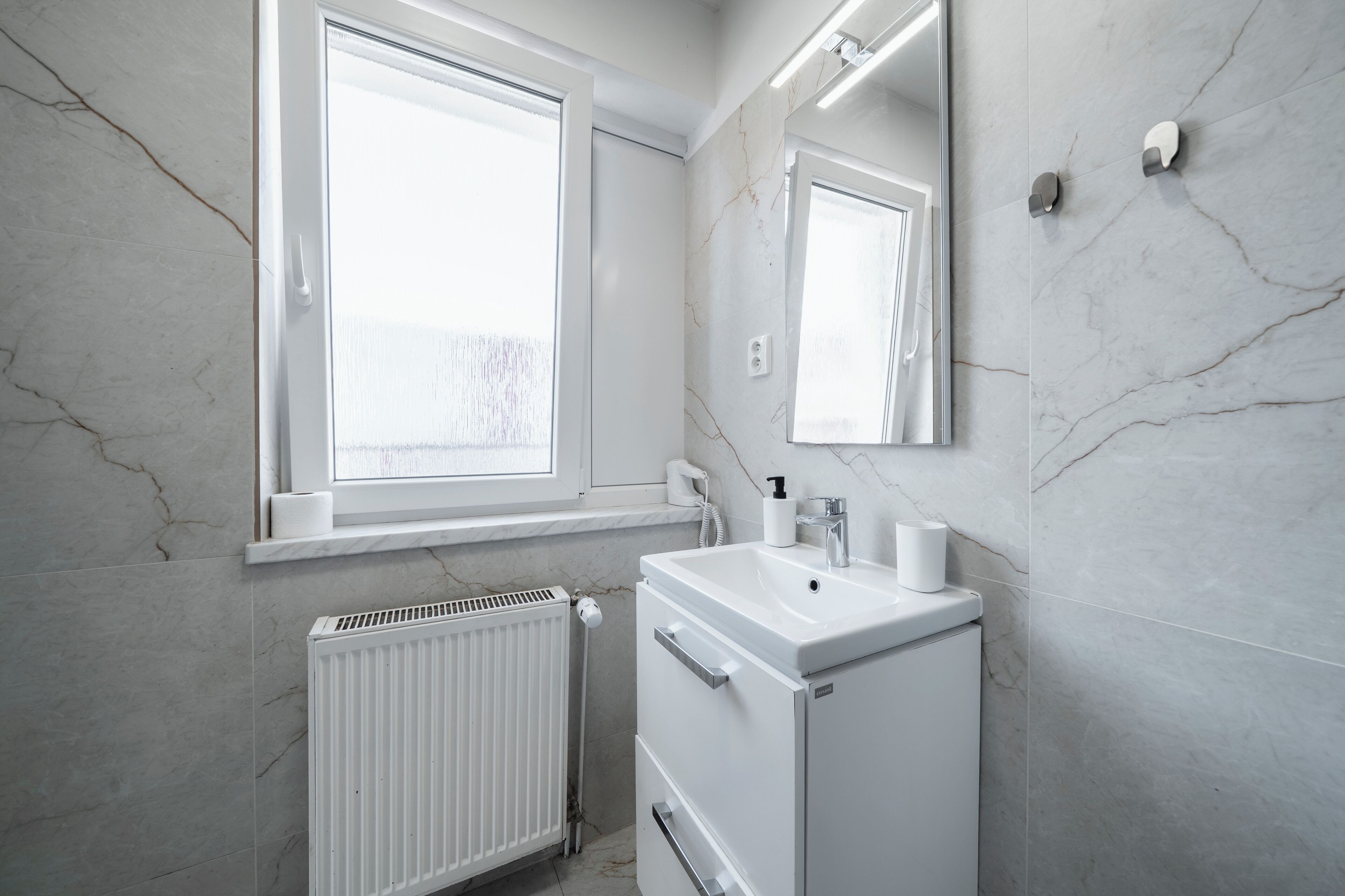 Un baño con lavamanos blanco, espejo y radiador.