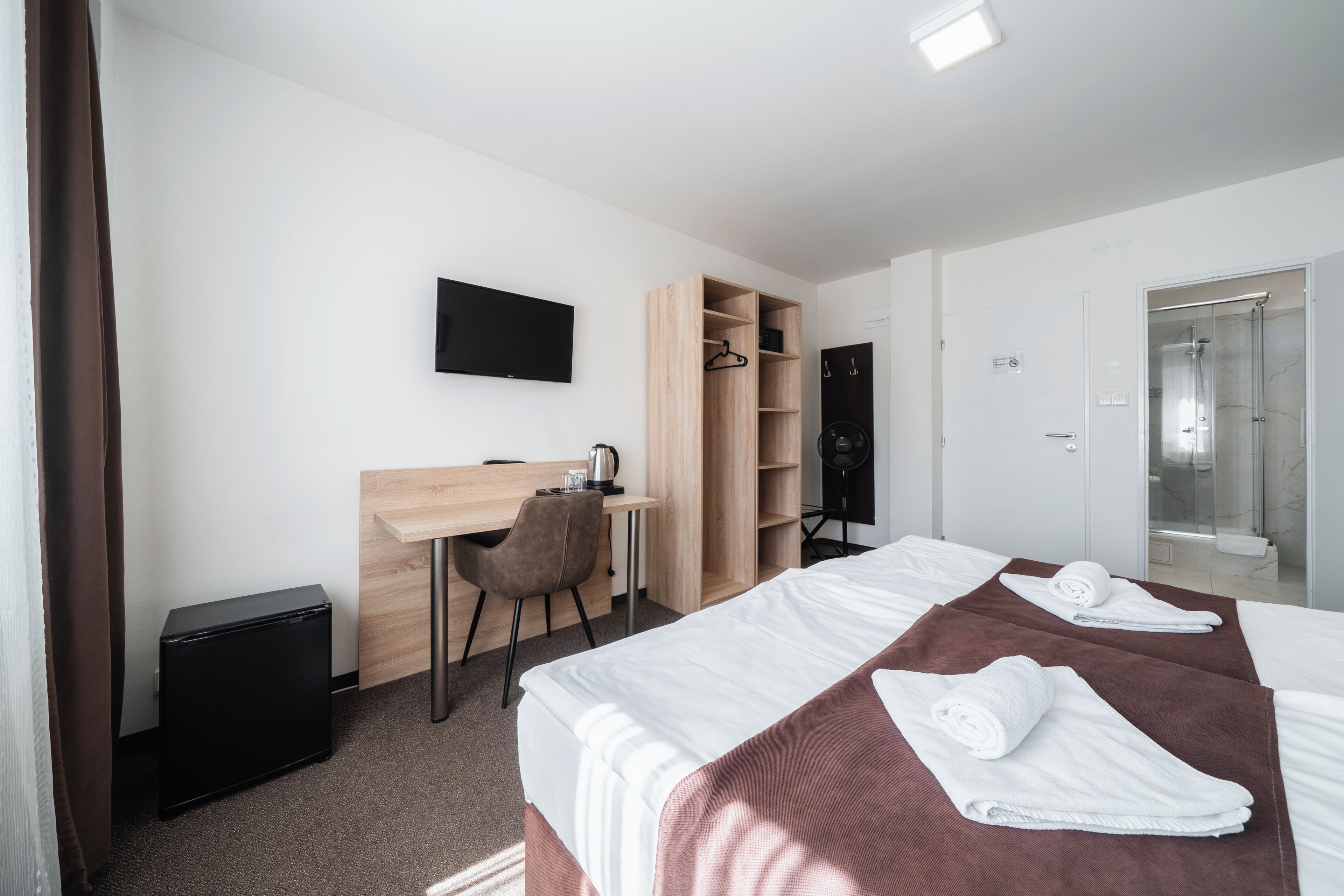Ein Hotelzimmer mit zwei Betten, einem Schreibtisch, einem Stuhl, einem Fernseher und einem Duschbereich.