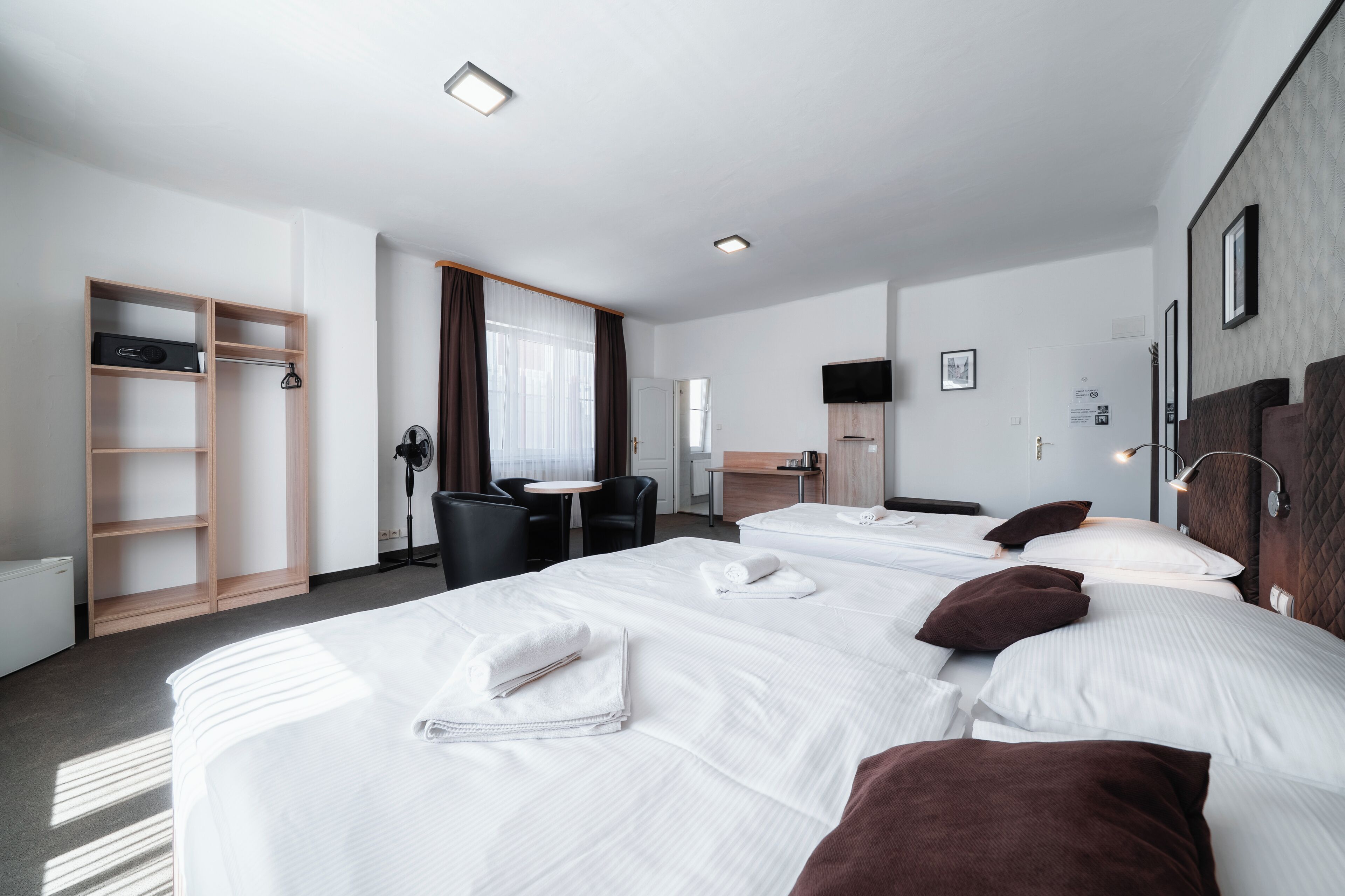 A hotel room with three beds, a desk, a chair, a wardrobe, and a television.