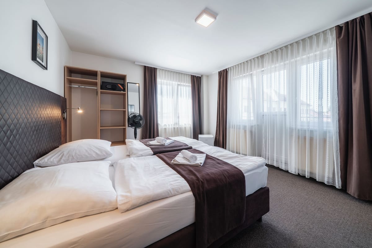A hotel room with two beds, a wardrobe, a mirror, and a window with curtains.
