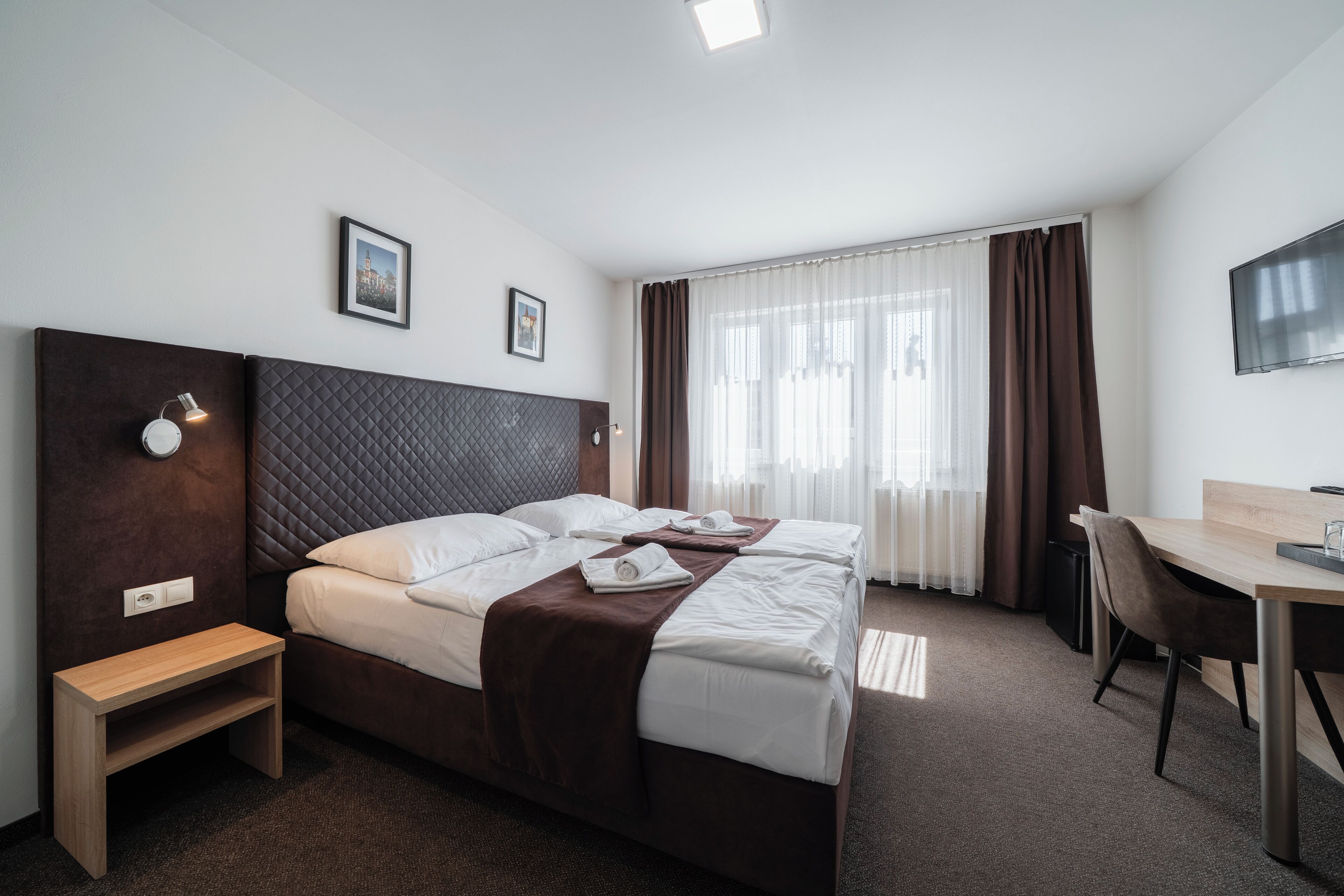A hotel room with a large bed, a desk, a chair, and a TV on the wall.