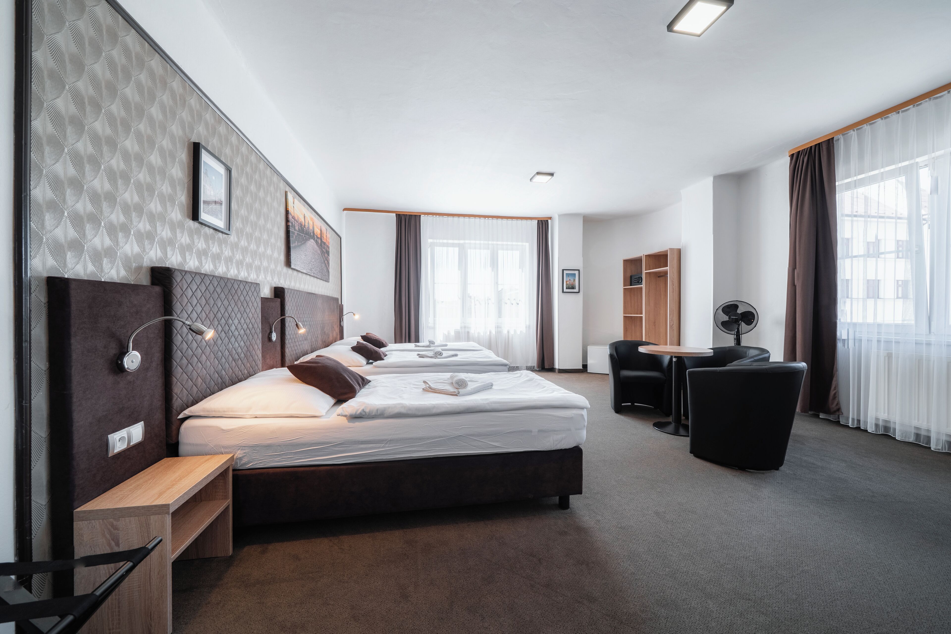 Quarto de hotel moderno com uma cama grande, mesas de cabeceira, escrivaninha e uma cadeira.
