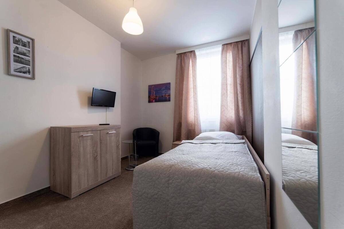 A hotel room with a bed, a TV, a desk, a chair, and a window with curtains.