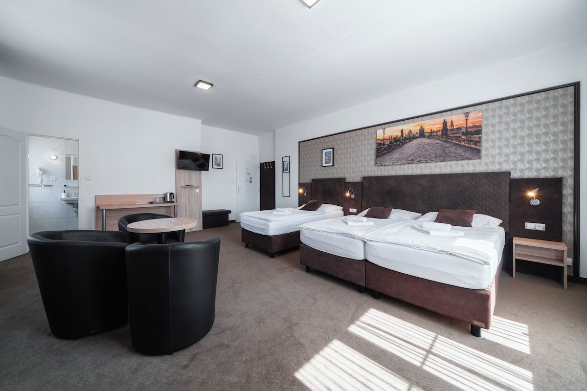 A hotel room with a large bed, two smaller beds, a dining table, and a seating area.