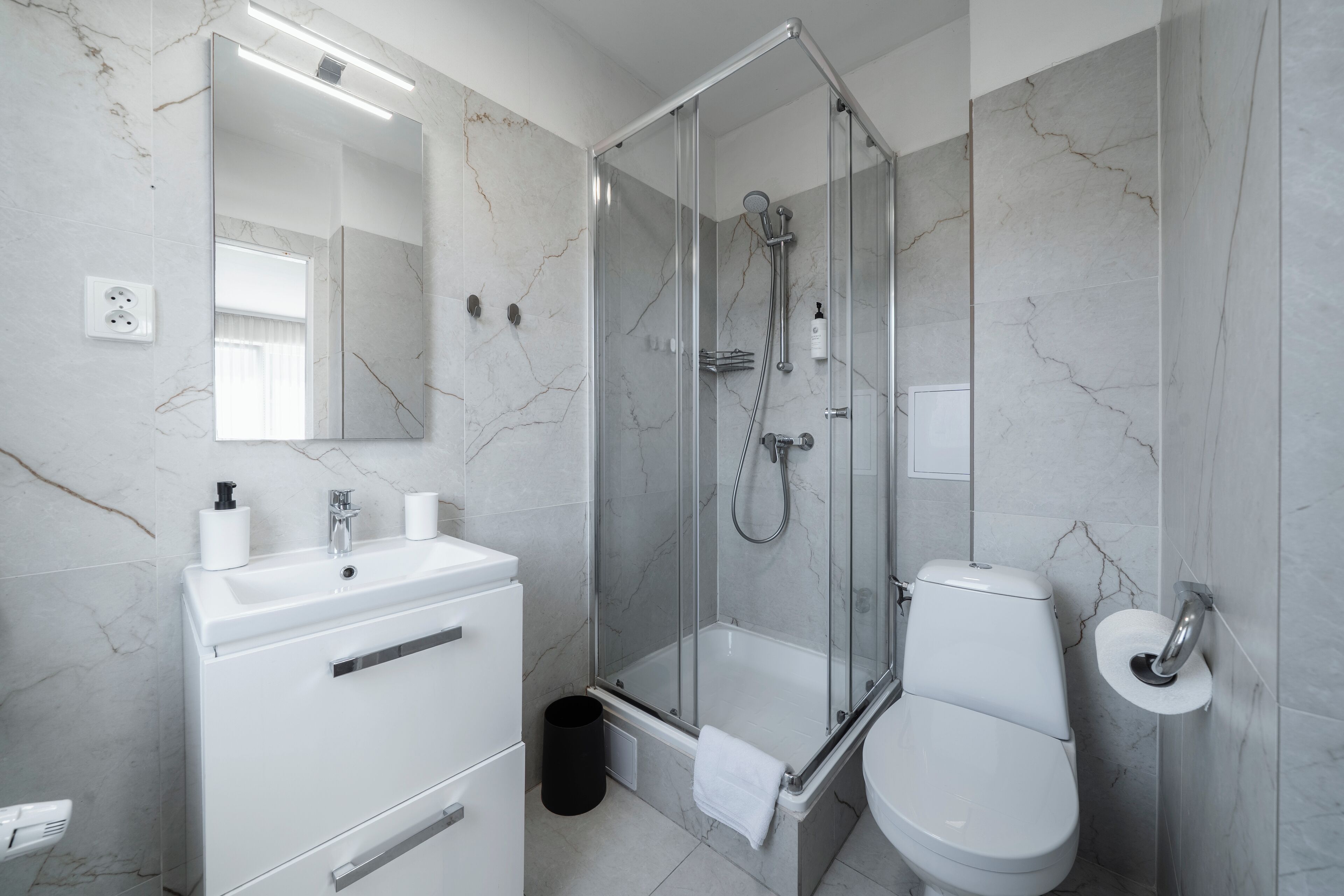 A modern bathroom with a glass-enclosed shower, a white sink, and a toilet.