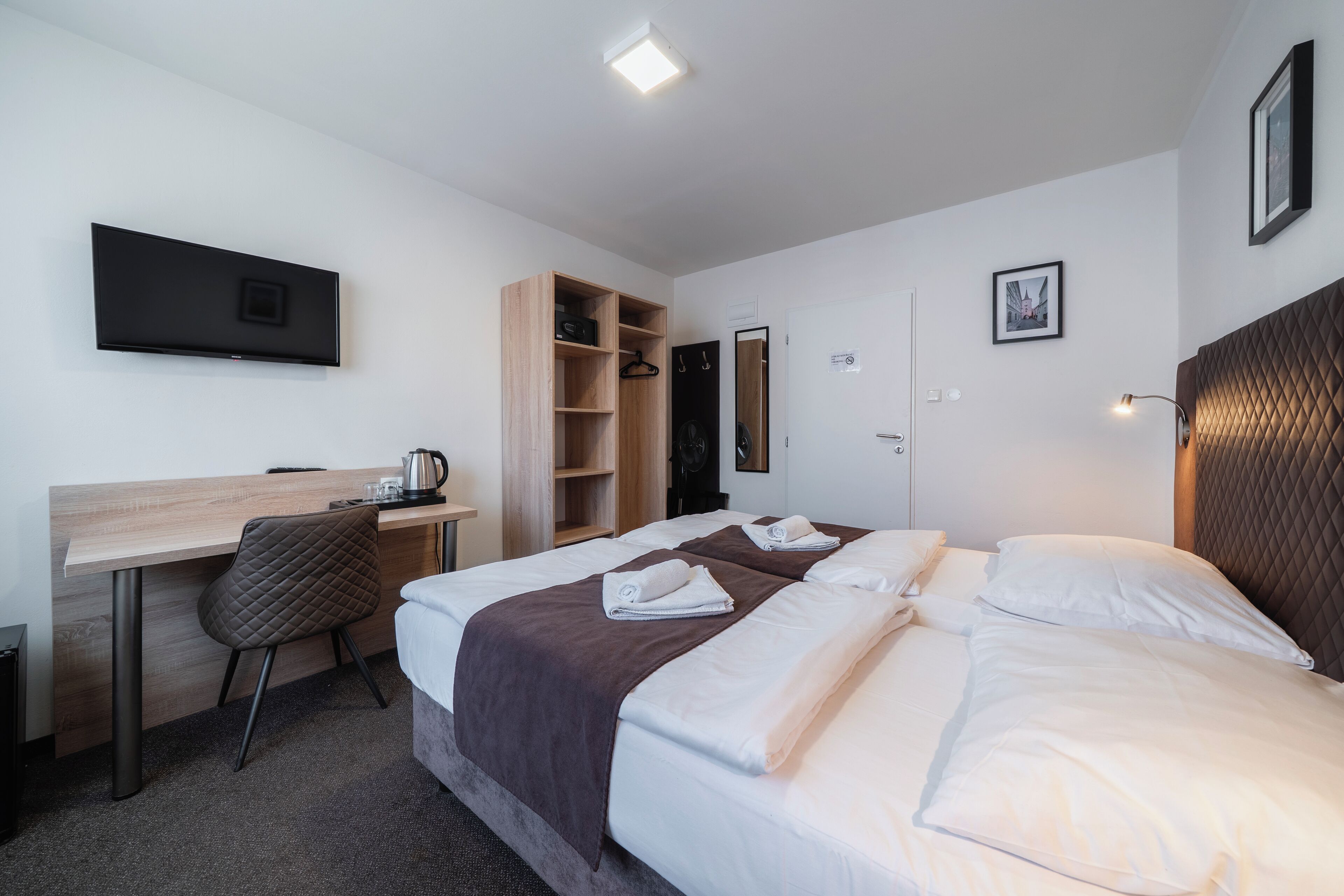 A hotel room with a bed, a desk, a chair, a TV, and a wardrobe.