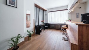 A modern hotel room with a wooden floor, a bar area, a seating area with chairs, a potted plant, and a window with curtains. - Penzion Homér Slaný (Slany)