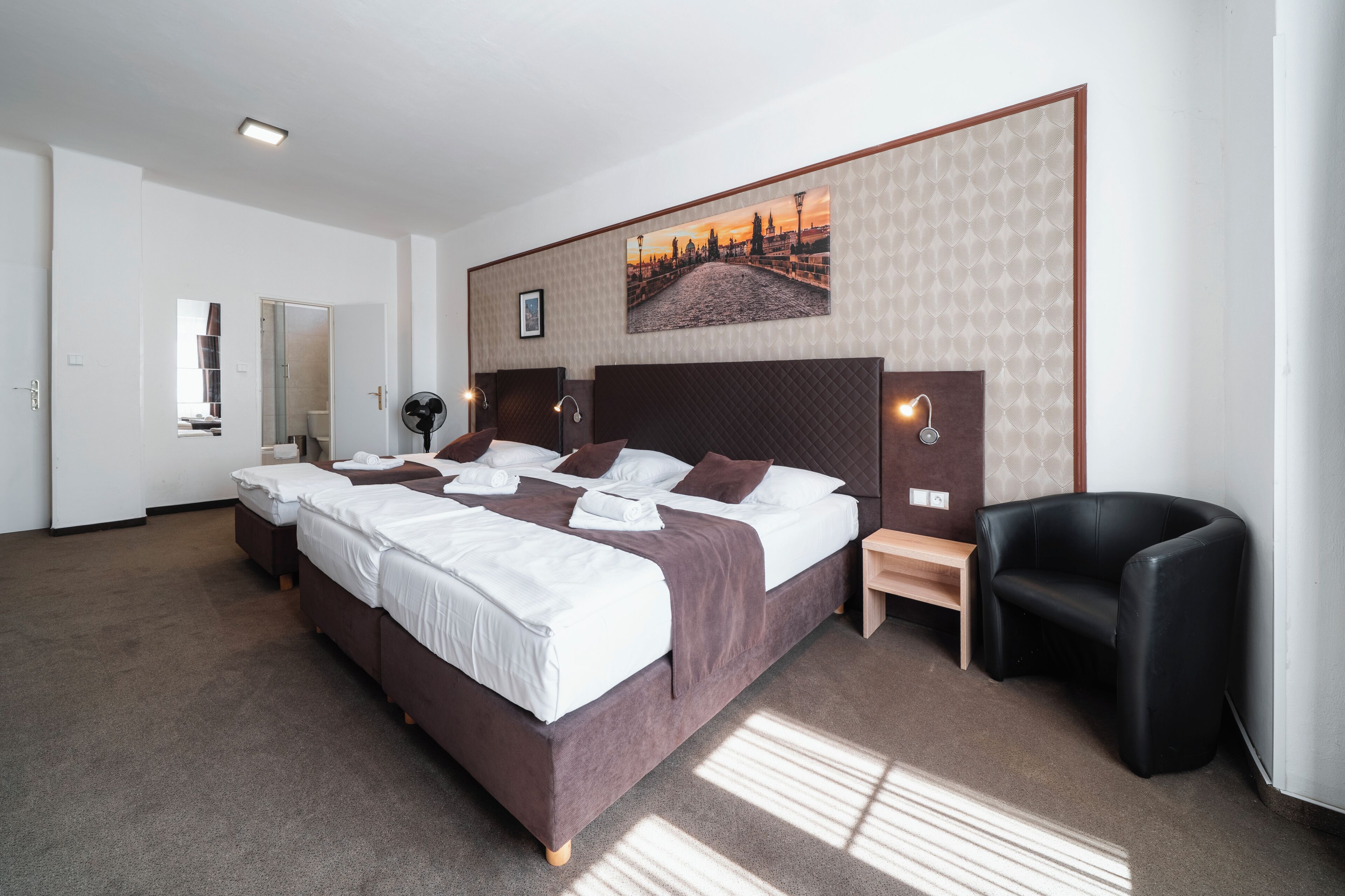 A hotel room with a large bed, a bedside table, a chair, and a wall-mounted picture.