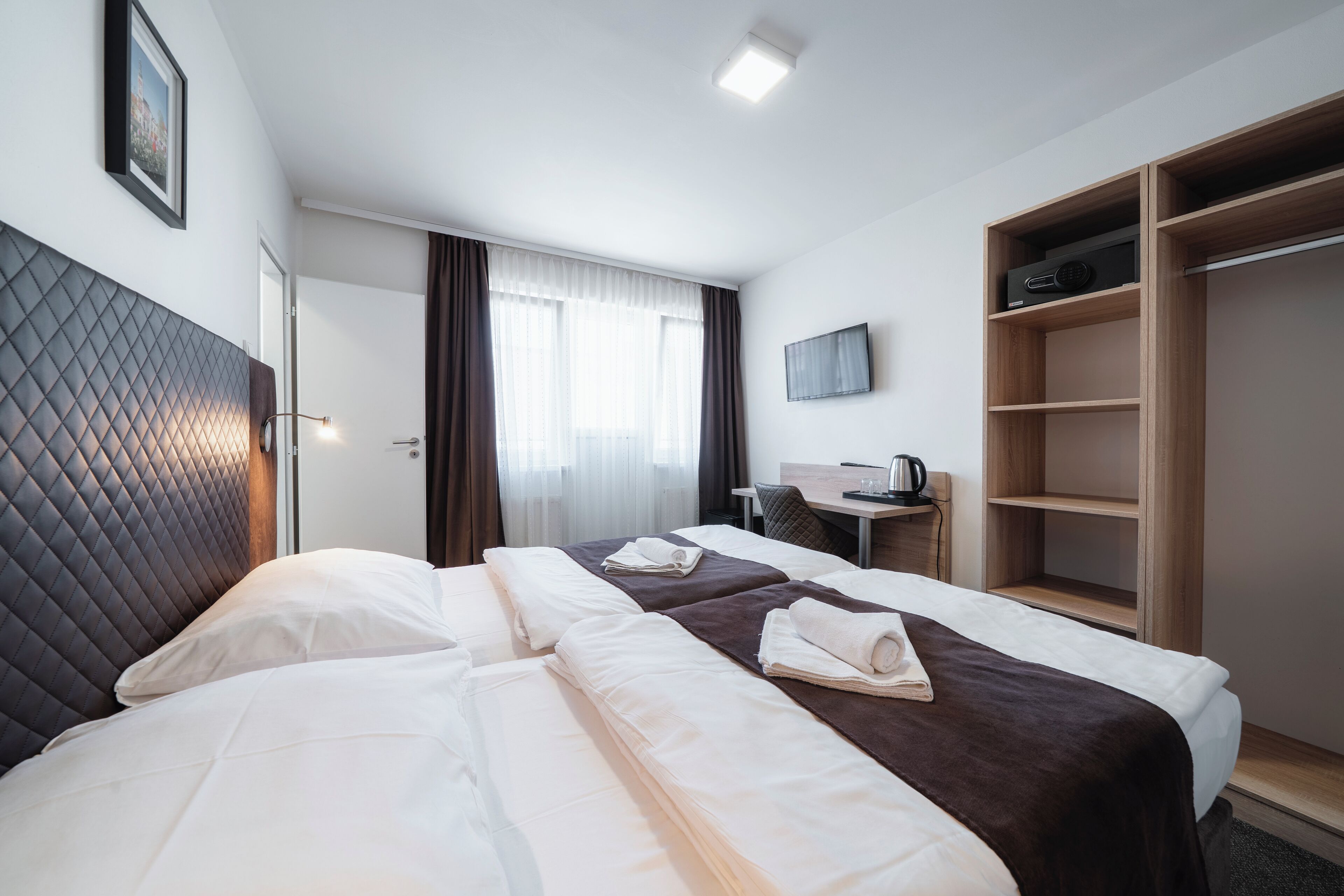 A hotel room with two beds, a desk, a TV, and a wardrobe.
