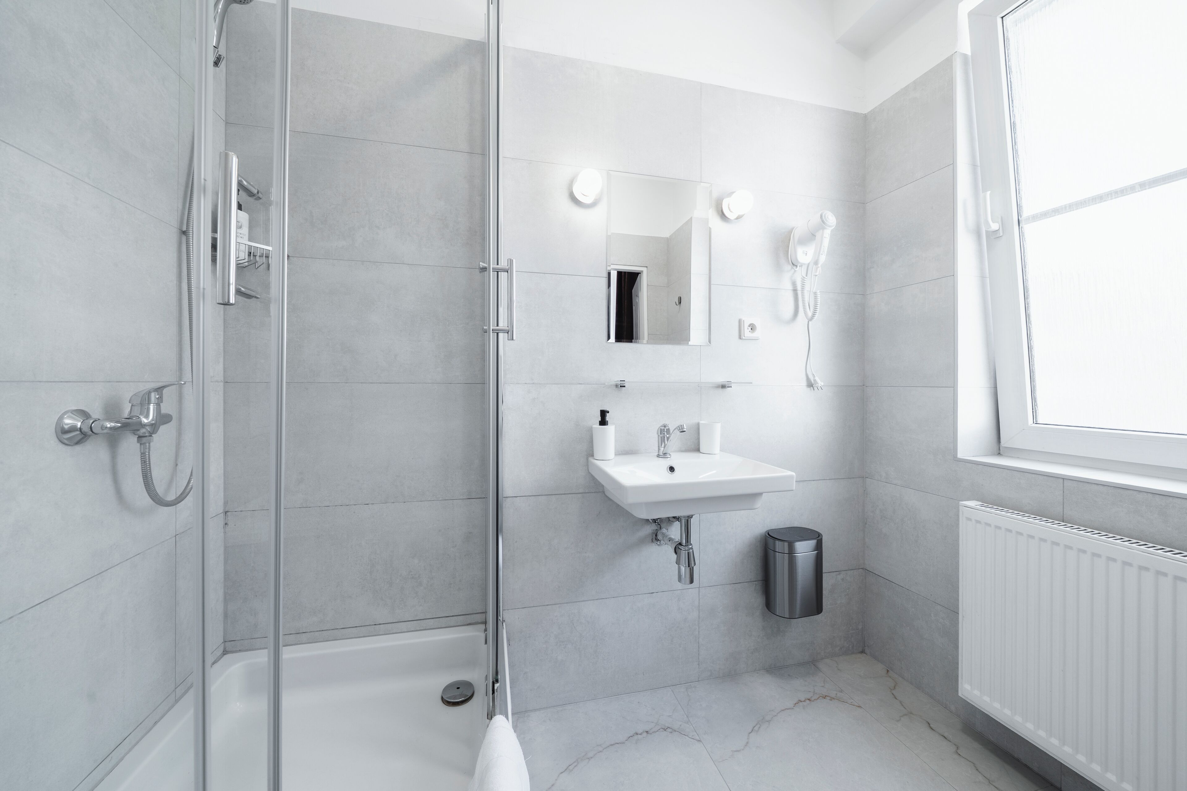 Een moderne badkamer met een douche met glazen wand, een witte wastafel en een spiegel erboven.