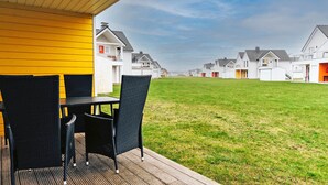Una terraza con mobiliario exterior que da a un área verde y hileras de casas blancas.