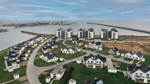 Un barrio residencial con casas dispuestas en semicírculo alrededor de una avenida central, con una masa de agua y un puente al fondo.