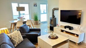 Una sala de estar moderna con un sofá, una mesa de centro, televisor y chimenea. Hay un comedor con sillas y una mesa.