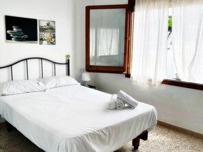 Una cama bien tendida con sábanas blancas, una lámpara de noche y un espejo en la pared.