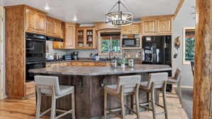 Une cuisine spacieuse avec des meubles en bois, un grand îlot central doté de tabourets, des appareils en acier inoxydable et un lustre.