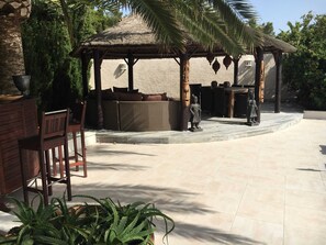 A covered outdoor seating area with a thatched roof, cushioned seating, and a statue. - Casa Verde, cozy holiday home with private heated pool in Javea (Jávea)
