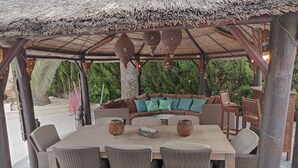 A covered outdoor seating area with wicker furniture, a thatched roof, and a view of greenery in the background. - Casa Verde, cozy holiday home with private heated pool in Javea (Jávea)