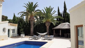 A swimming pool with lounge chairs, palm trees, and a thatched-roof structure. - Casa Verde, cozy holiday home with private heated pool in Javea (Jávea)