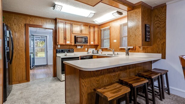 A kitchen with wooden cabinets, a microwave, a stove, and a sink. There are three wooden stools at the island. - Dogs Give us 5 Stars! 3BR, Large Fenced Yard, Rustic Escape (Orange Park)