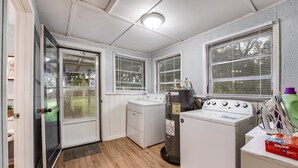 A laundry room with a washer, dryer, and water heater. There are windows with blinds, a door, and a small rug on the floor. - Dogs Give us 5 Stars! 3BR, Large Fenced Yard, Rustic Escape (Orange Park)