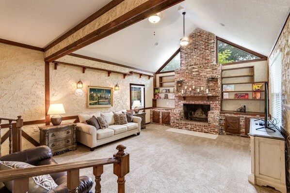 A spacious living room with a fireplace, a sofa set, and a bookshelf.