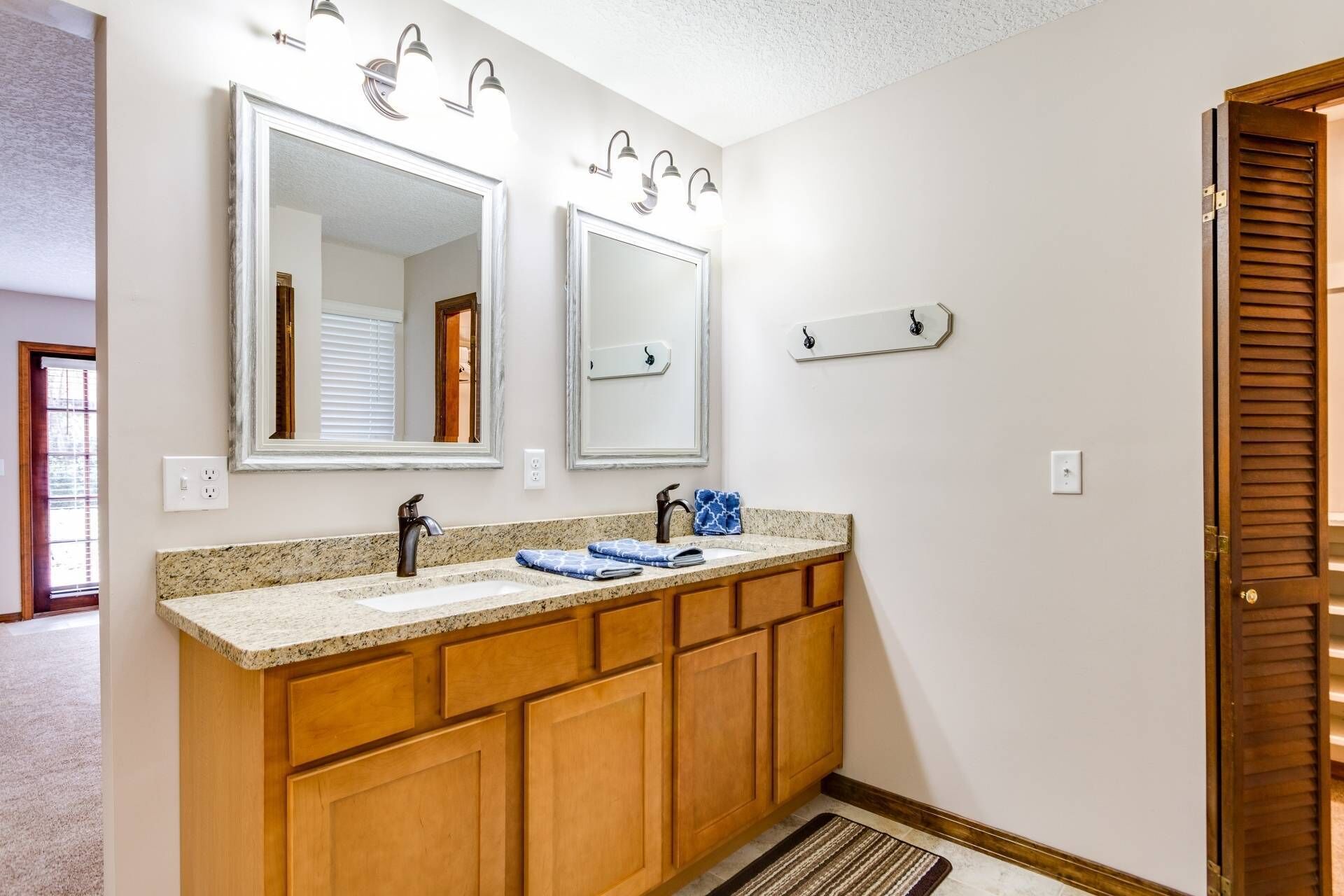 A bathroom with a double vanity, two wall-mounted mirrors, a granite countertop, wooden cabinets, and a door with a wooden panel.