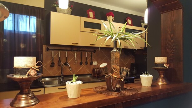 Una cocina con armarios de madera, un lavamanos y varios utensilios de cocina colgando en la pared. Hay tres jarrones decorativos sobre la encimera.