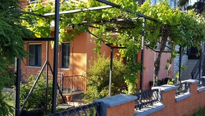 Un edificio con balcón, una pérgola cubierta de plantas trepadoras y una escalera.