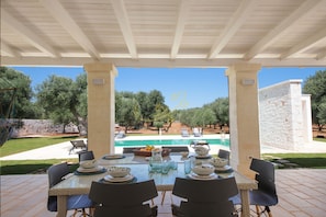 An outdoor dining area with a view of a swimming pool and olive trees.