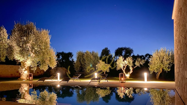 A serene outdoor pool area with trees and lounge chairs, surrounded by a stone wall. - TD Villa Ricchiari  | Design Villa with Heated Pool (Fasano)