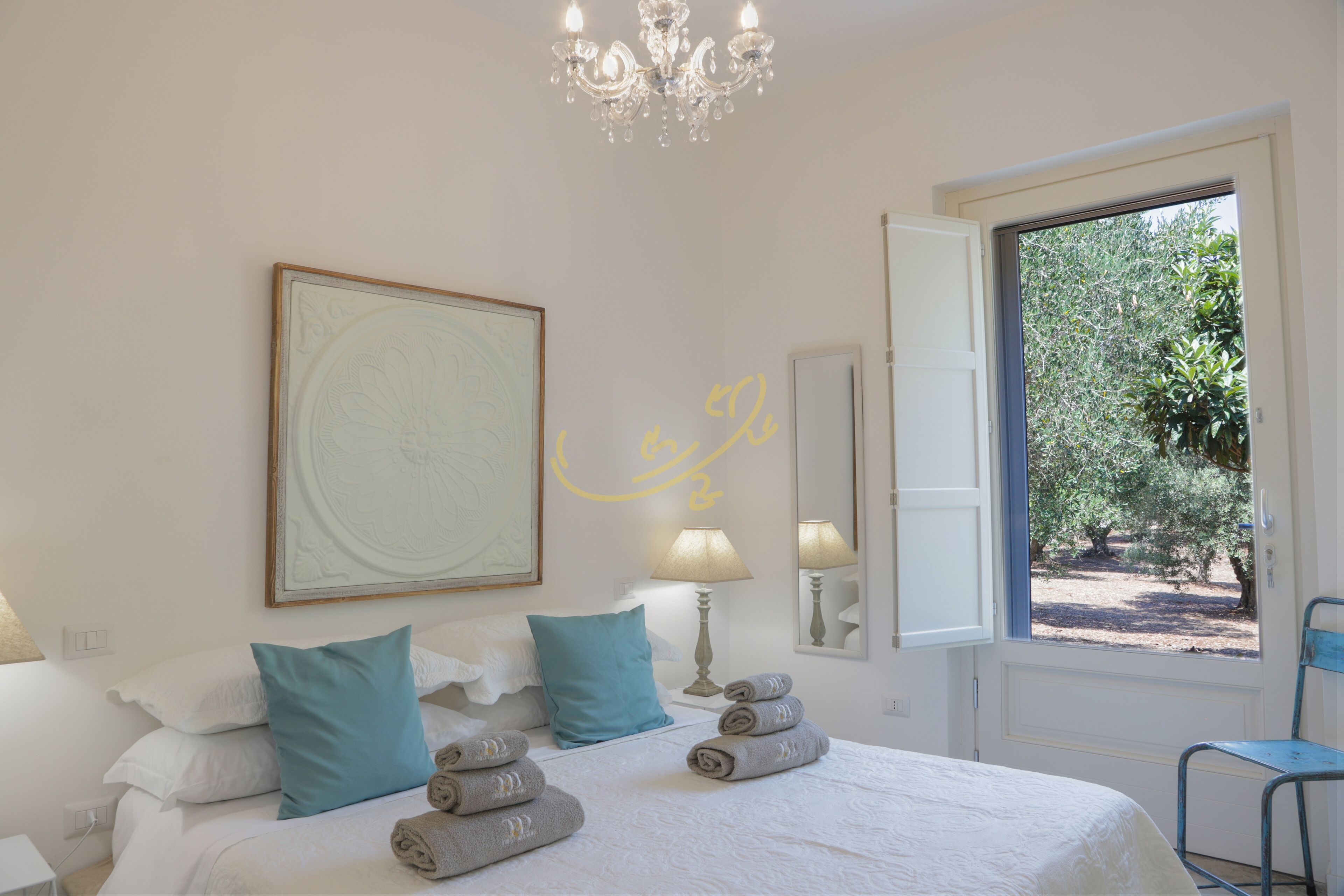 Un dormitorio con cama, almohadas, una araña, una ventana y una puerta.