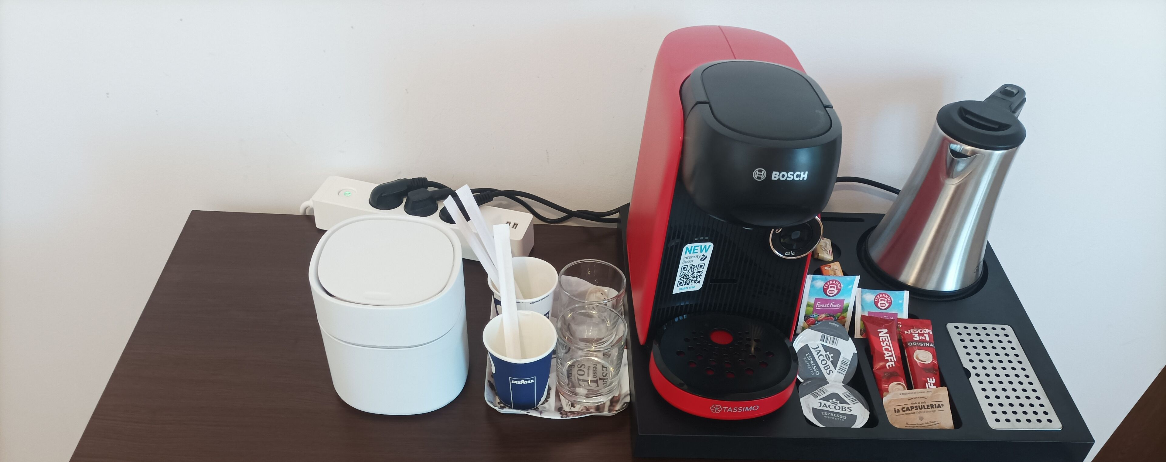 A coffee maker, a water bottle, a cup, and some coffee pods on a table.